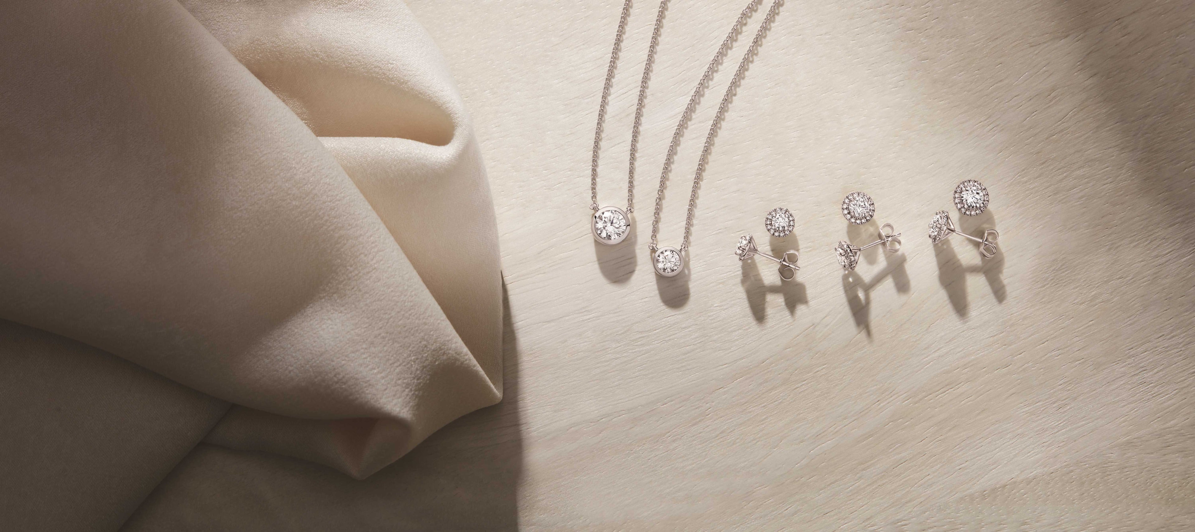 Diamond pendant necklaces and stud earrings displayed on neutral fabric