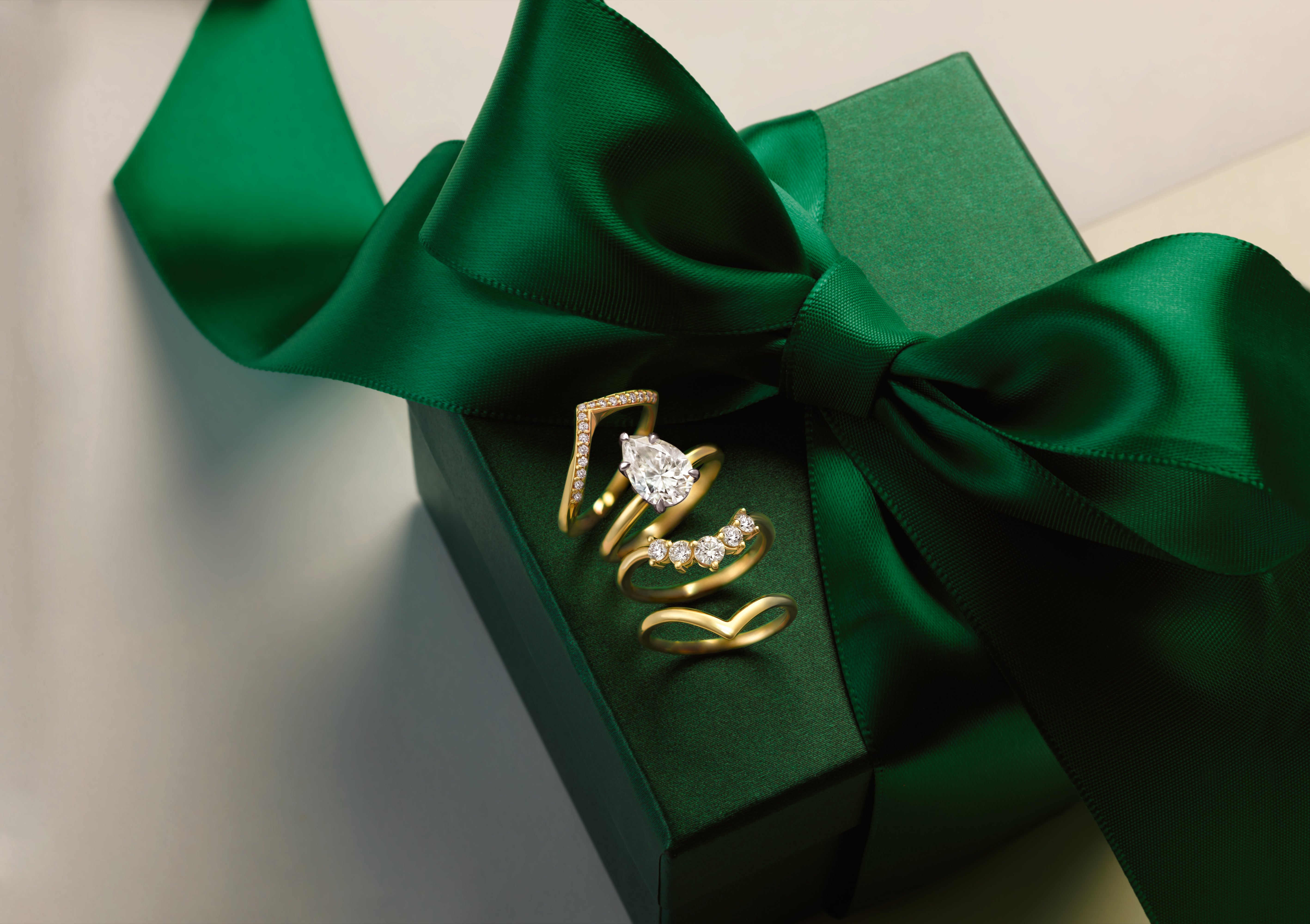Pear-shaped diamond ring and coordinating gold bands on a green jewelry box