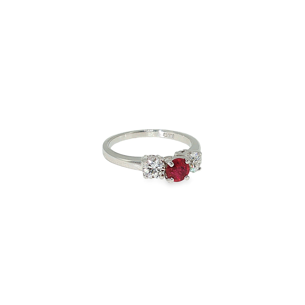 Three-stone ruby and diamond ring with a round red ruby center and two round brilliant diamond side stones in 14K white gold.