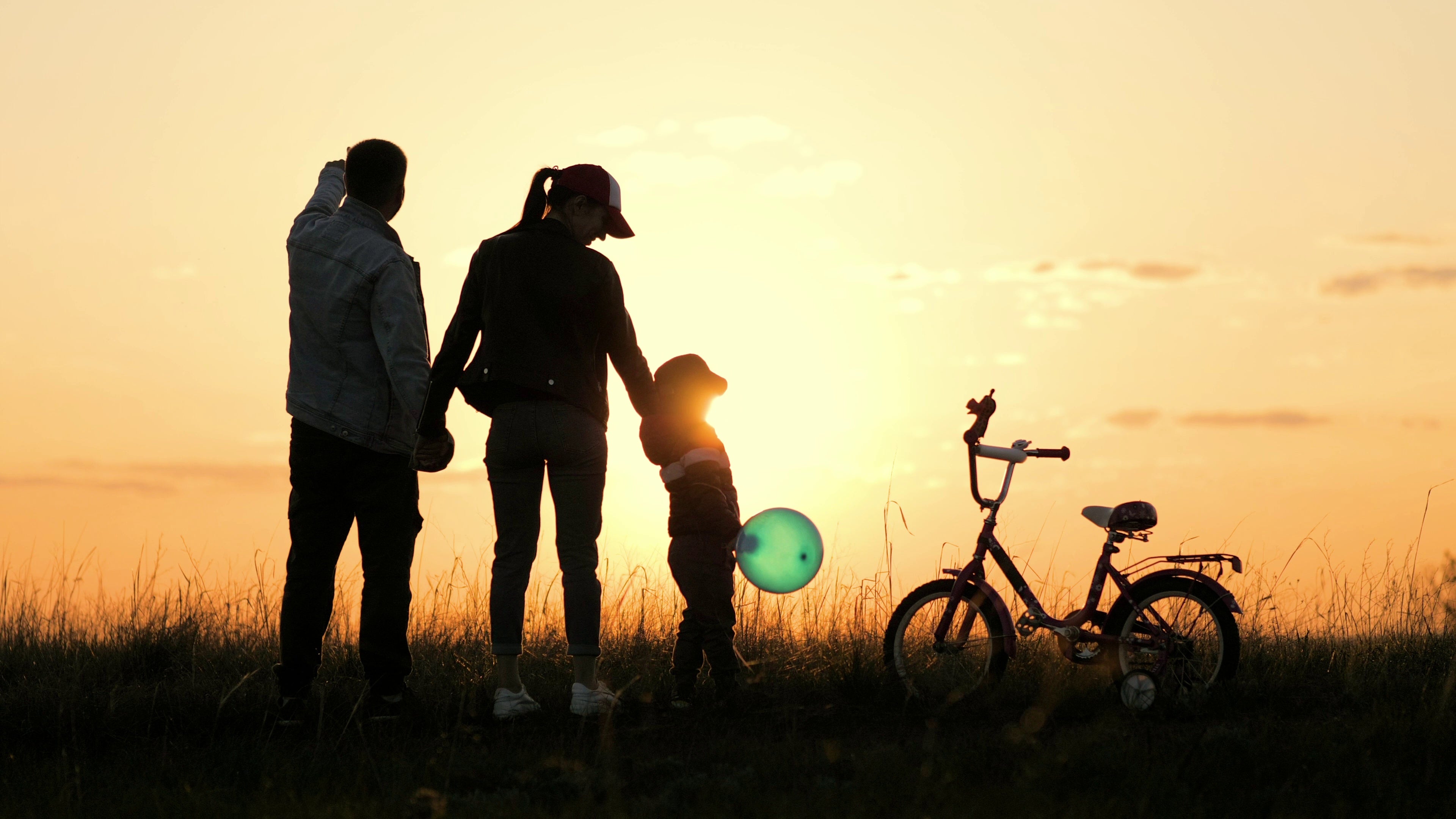 Silhouette of a family with a child and bicycle against a sunset sky.