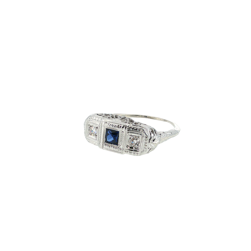 14K white gold filigree ring with a princess-cut blue synthetic sapphire and two round diamond accents.