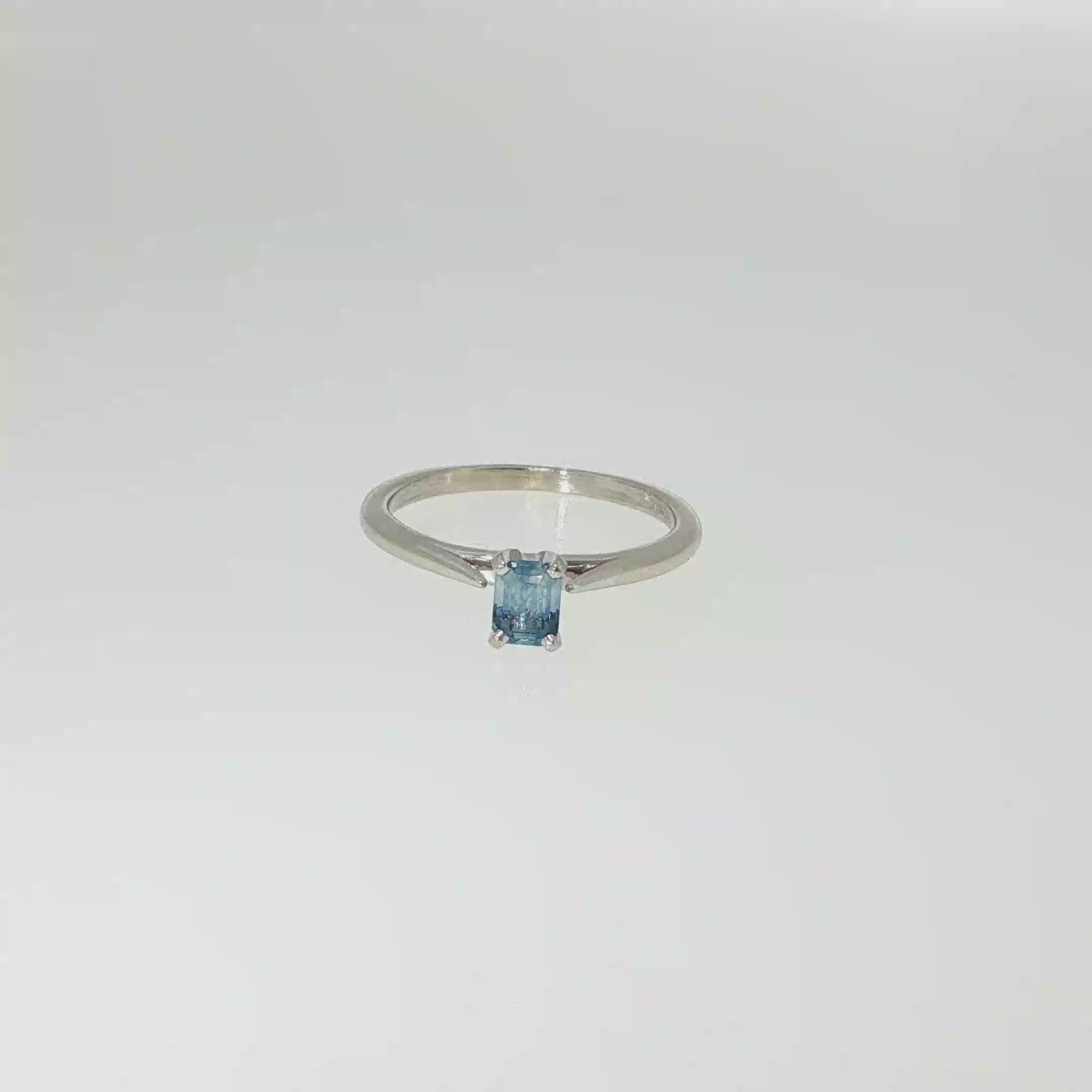 14K white gold solitaire ring with a light blue emerald-cut sapphire in a four-prong setting.