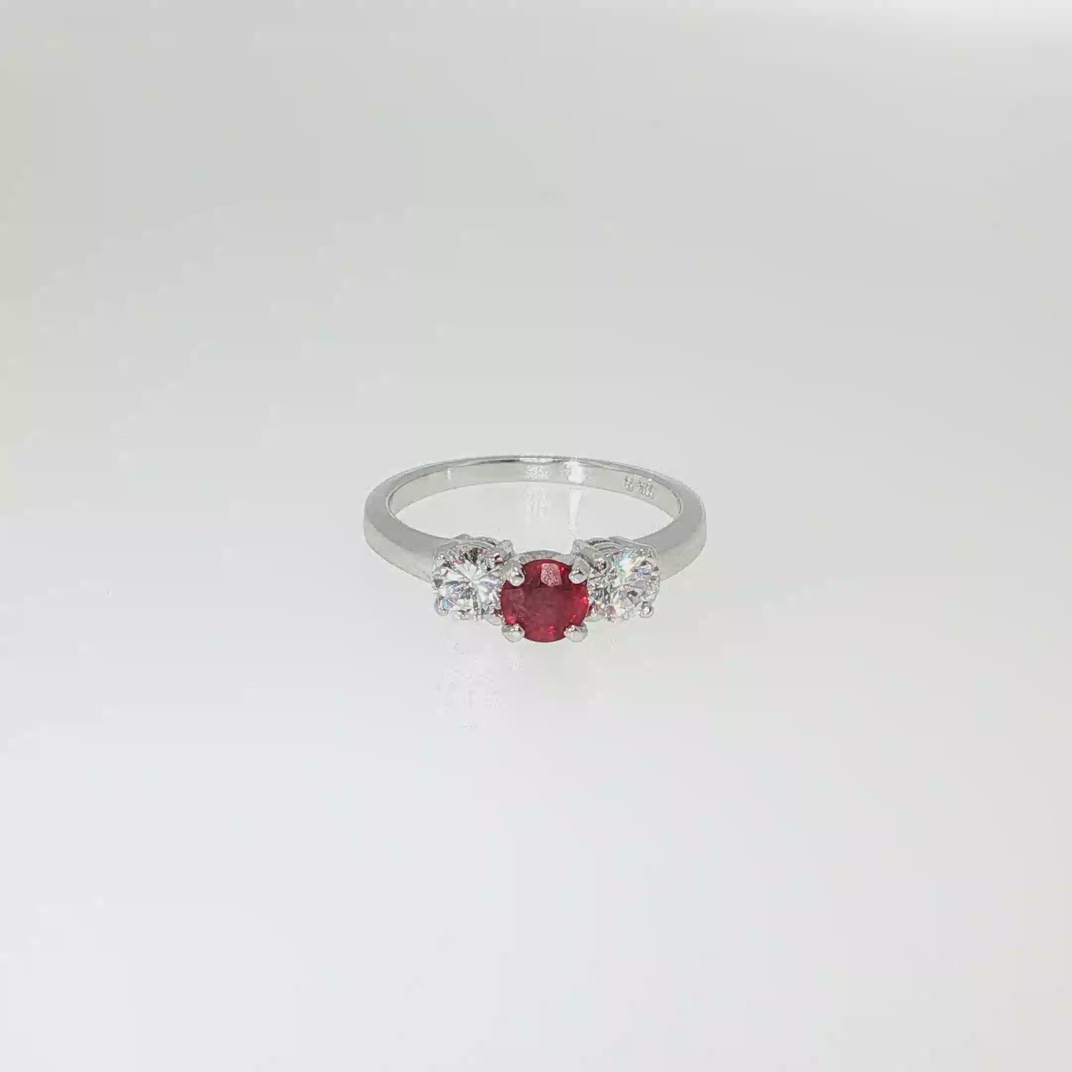 Three-stone ruby and diamond ring with a round red ruby center and two round brilliant diamond side stones in 14K white gold.