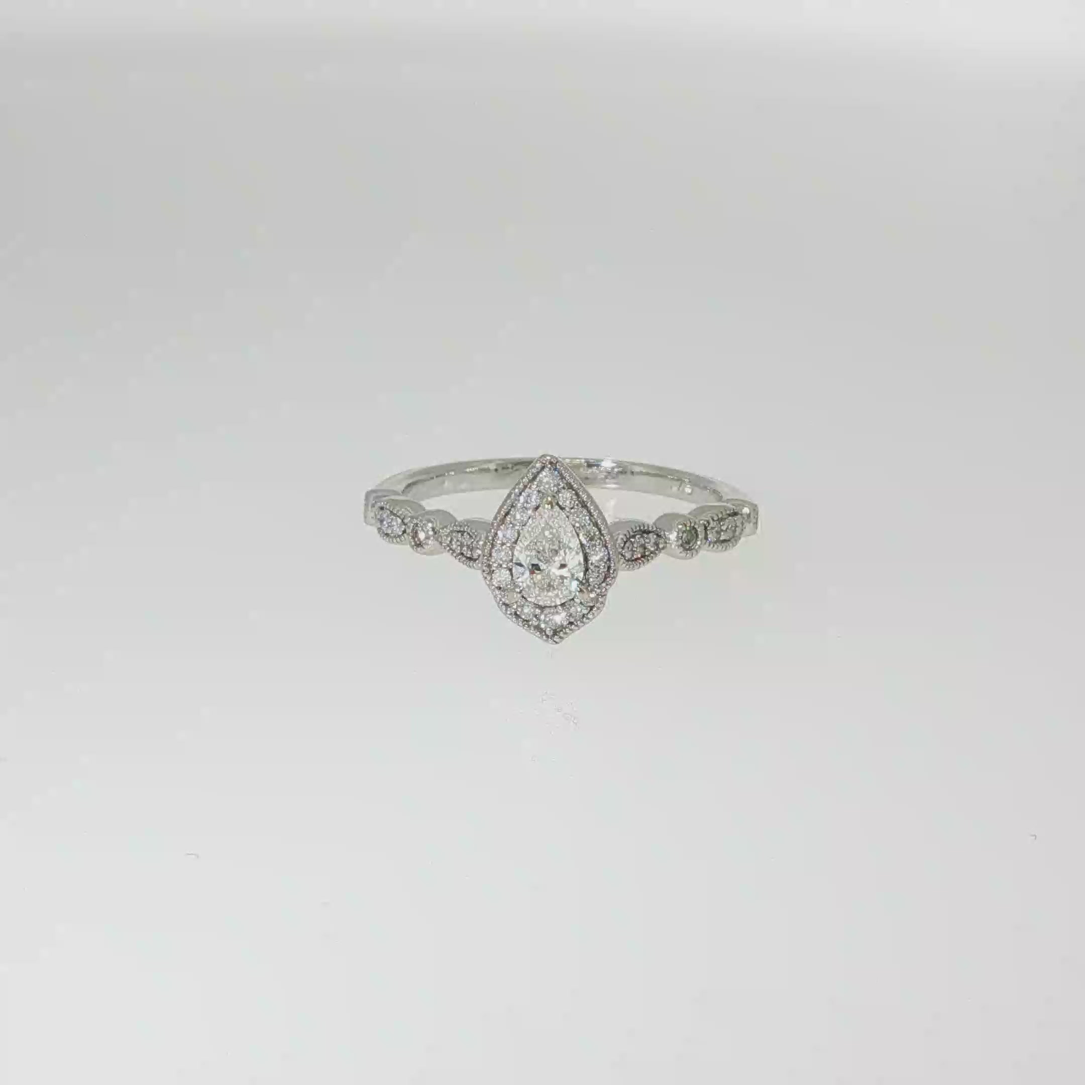 Pear-shaped diamond halo engagement ring in 14K white gold with round diamond accents along the band.